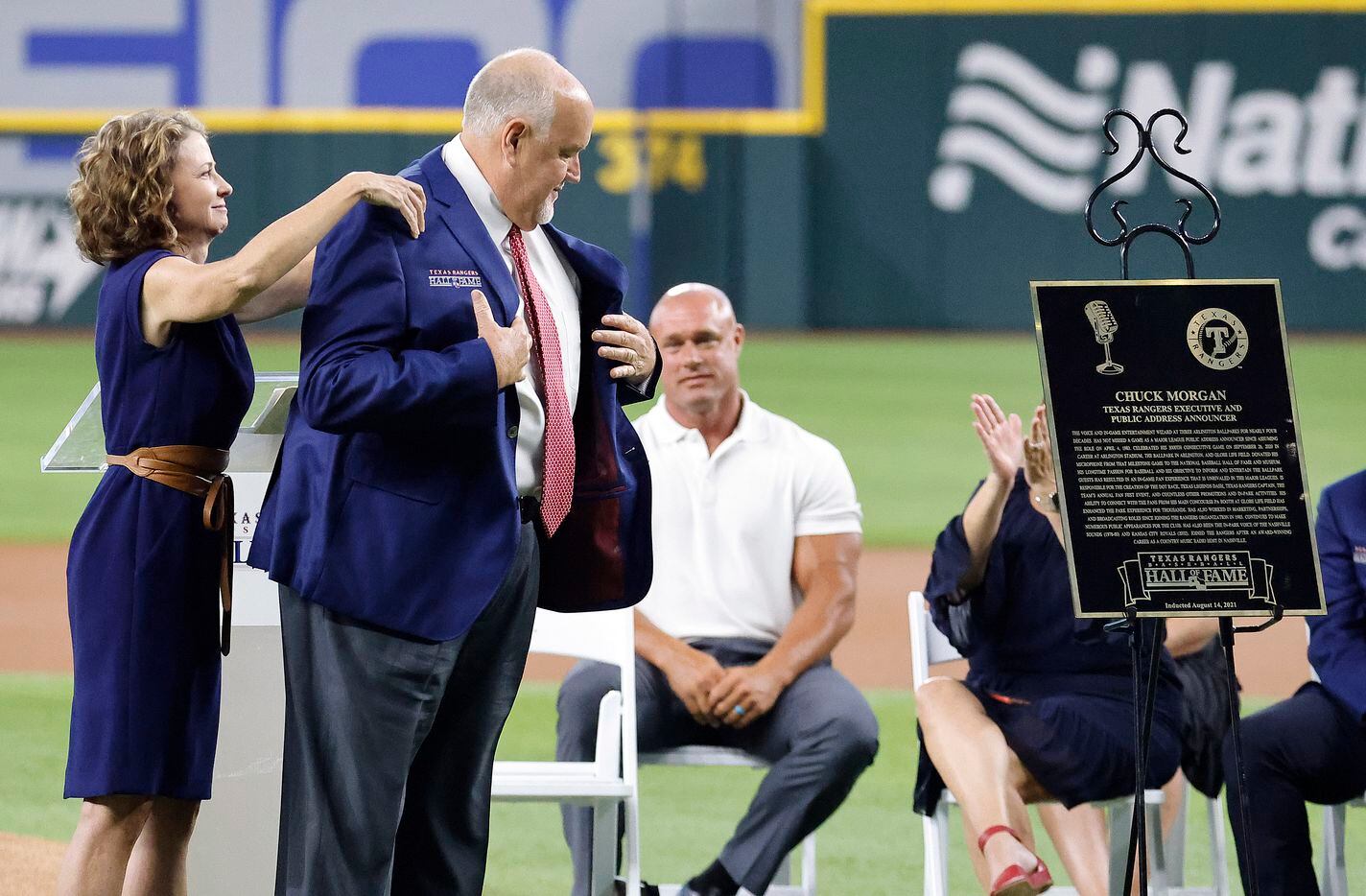 Texas Rangers executive vice president and public address announcer Chuck Morgan receives help with his blue jacket from his presenter and Rangers CFO Kellie Fischer during the Texas Rangers Baseball Hall of Fame induction ceremony at Globe Life Field in Arlington, Saturday, August 14, 2021.(Tom Fox/The Dallas Morning News)