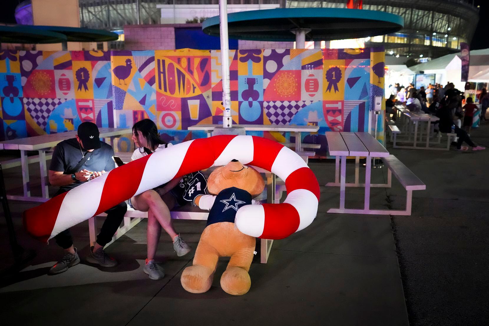 Fairgoers rest on a picnic table while covered in plush toys won on the midway on opening...