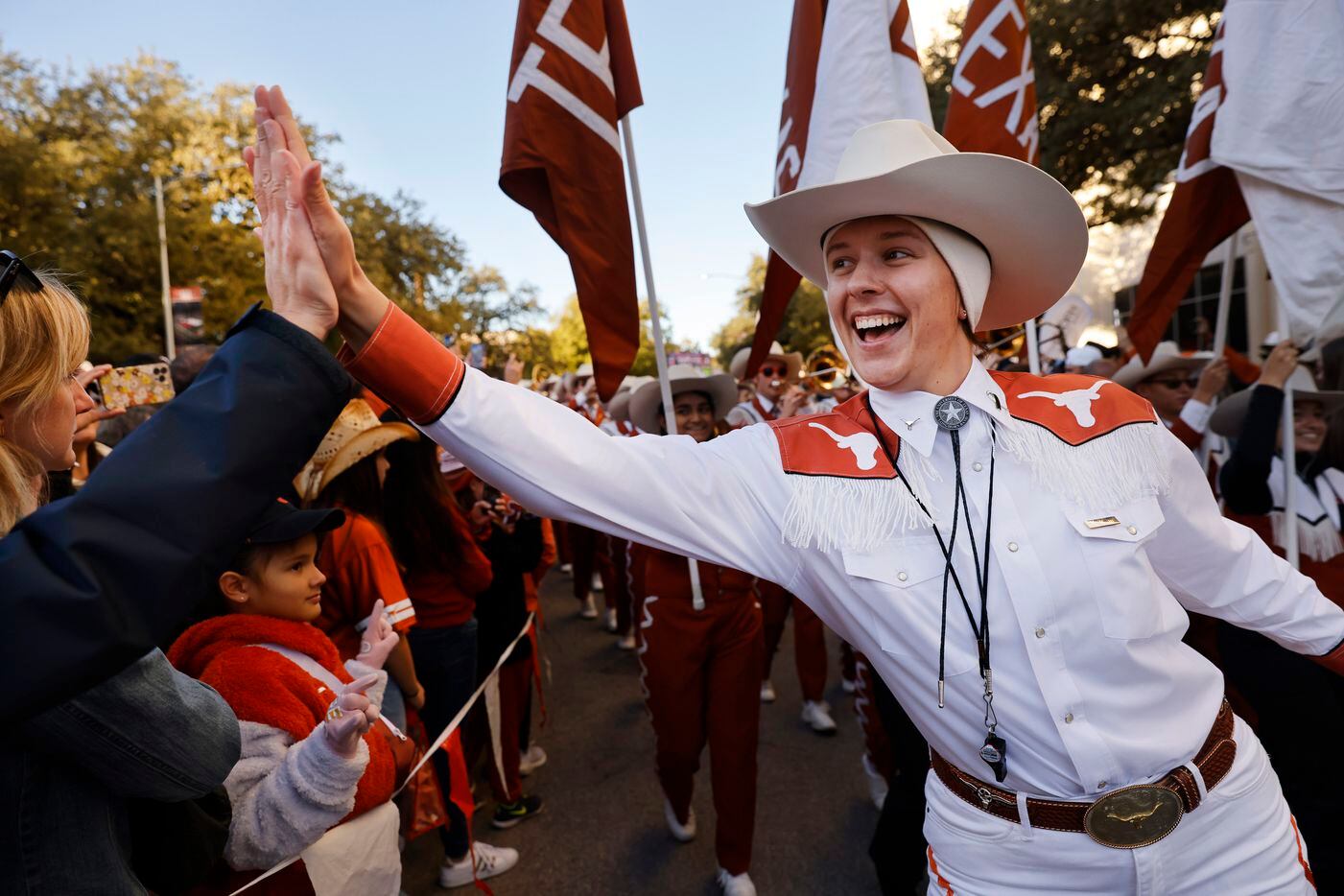 University of Texas Longhorn Band members slap hands with fans as they lead the football...