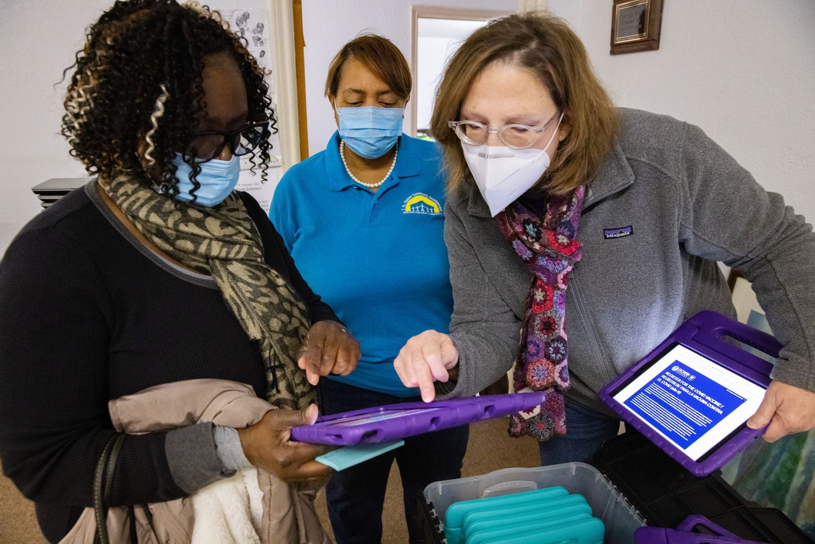 From left: Frenchell White, executive director Sherri Mixon  and Carrie Bhasin prepared iPads for vaccine registration Tuesday at T.R. Hoover community center in Dallas. People arriving for a food distribution were also signed up to get COVID-19 shots.