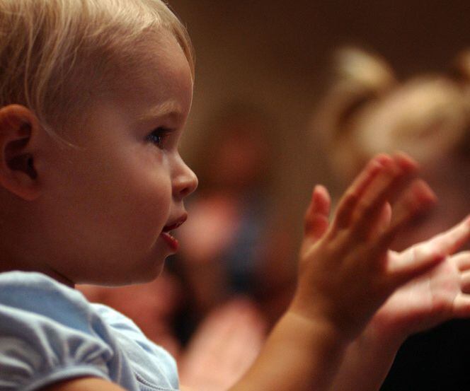 A toddler claps to the rythmn of a song.