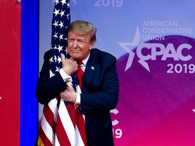 President Donald Trump hugs the American flag as he arrives on stage to speak at the Conservative Political Action Conference, CPAC 2019, in Oxon Hill, Md., on March 2, 2019.