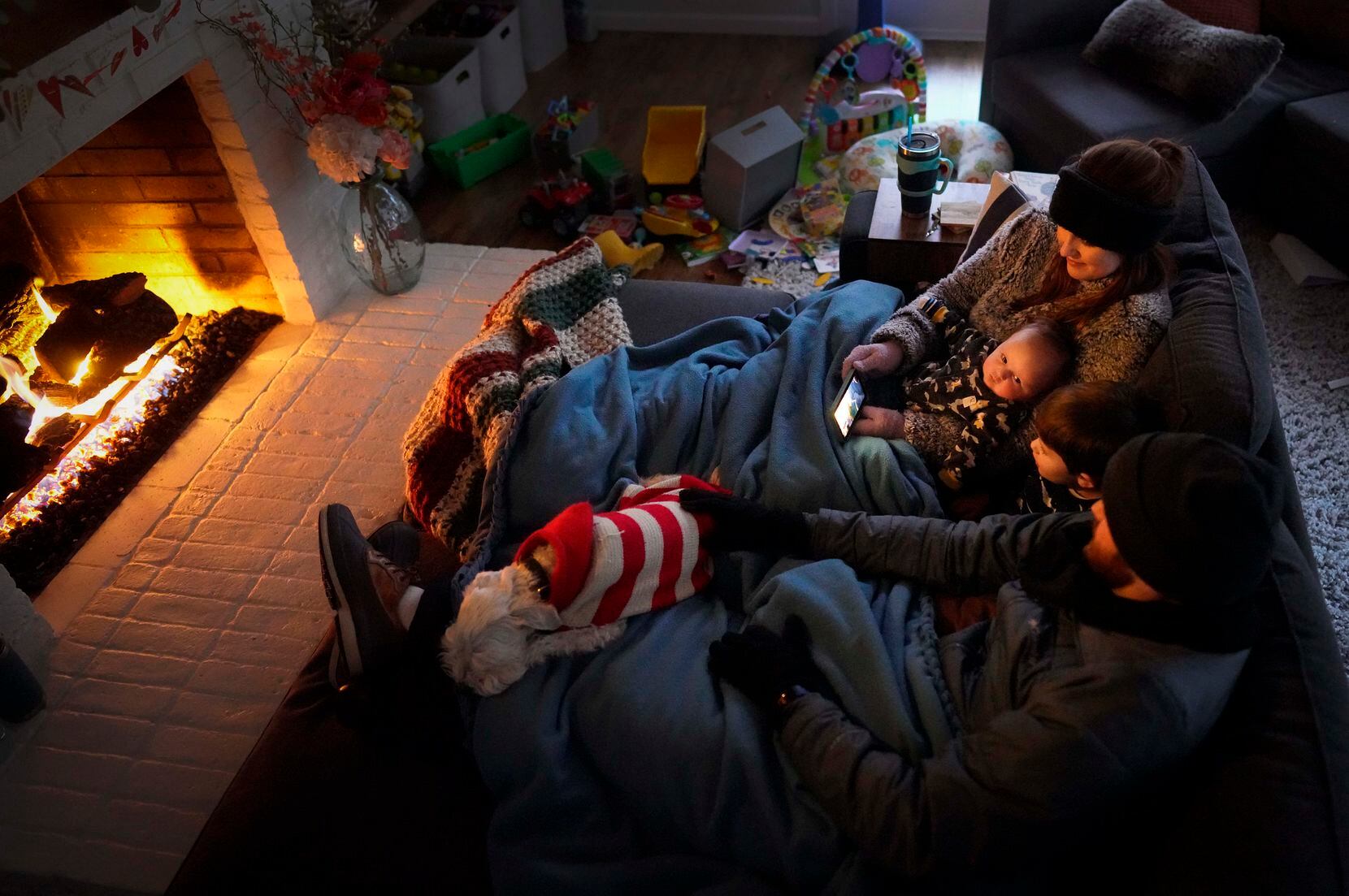 Dan Bryant and his wife, Anna, huddled by the fire with sons Benny, 3, and Sam, 12 weeks, and their dog Joey, who was wearing two doggie sweaters, in their home in Garland. The massive winter storm let the Bryants, along with millions of other Texans without power. 