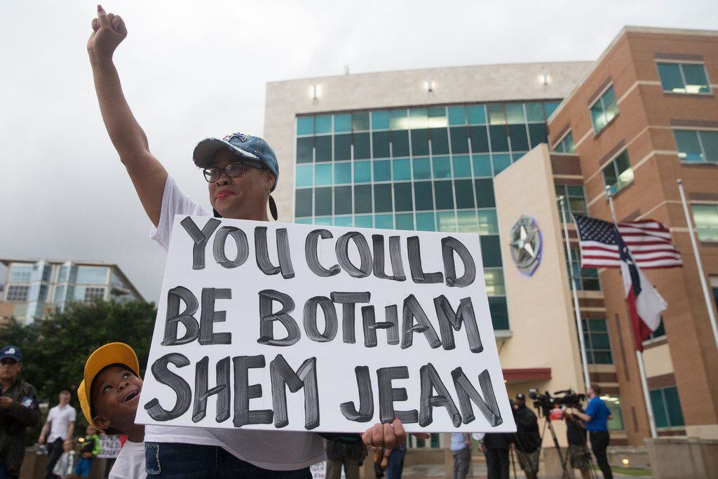 Dr. Pamela Grayson raises her fist as "Young King" Solomon Grayson, 6, peeks from behind her sign during a Mothers Against Police Brutality candlelight vigil for Botham Jean at the Jack Evans Police Headquarters in Dallas on Sept. 7.