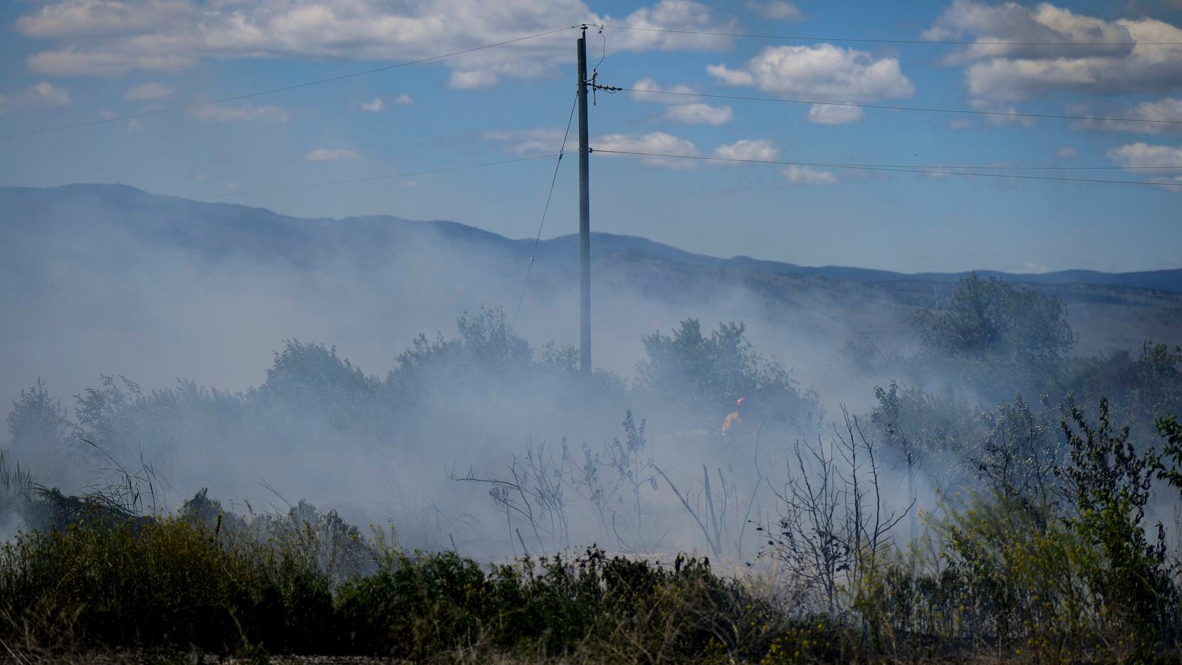 A firefighter directs water on a grass fire on an acreage behind a residential property in...
