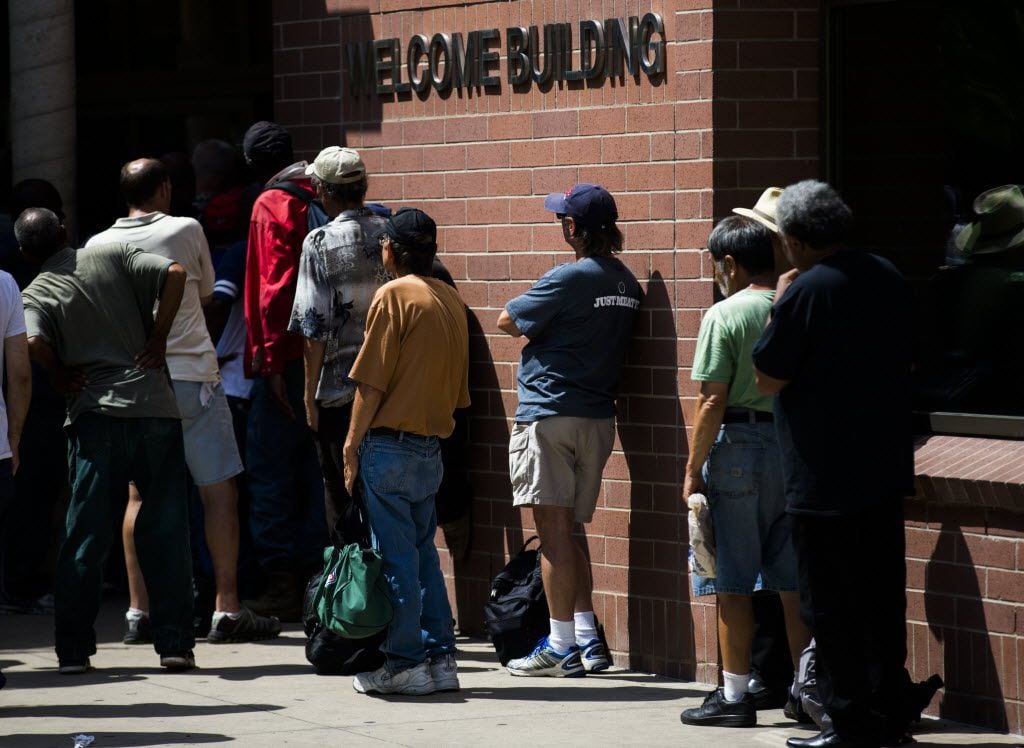 People wait in line at The Bridge Homeless Recovery Center on Corsicana Street in downtown...
