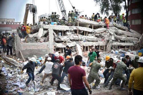 Rescatistas, soldados y voluntarios buscan sobrevivientes entre los escombros de un edificio...