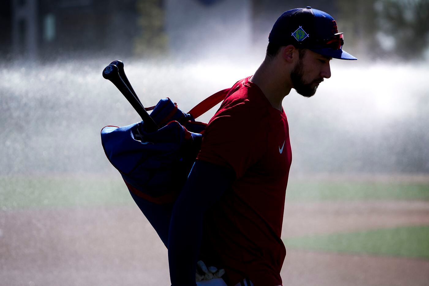 Texas Rangers outfielder Eli White heads to the practice fields as groundskeepers spray...
