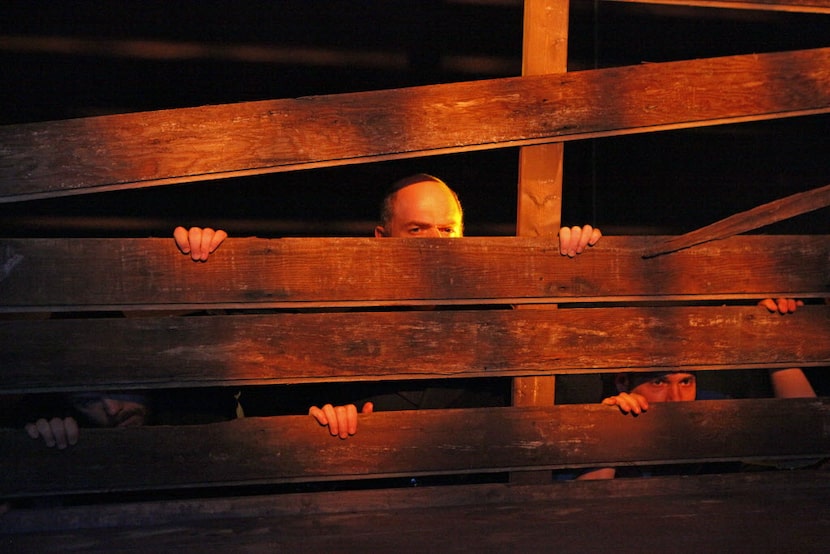 Characters peek through boards during a scene of theatre production of Booth, by Steven...