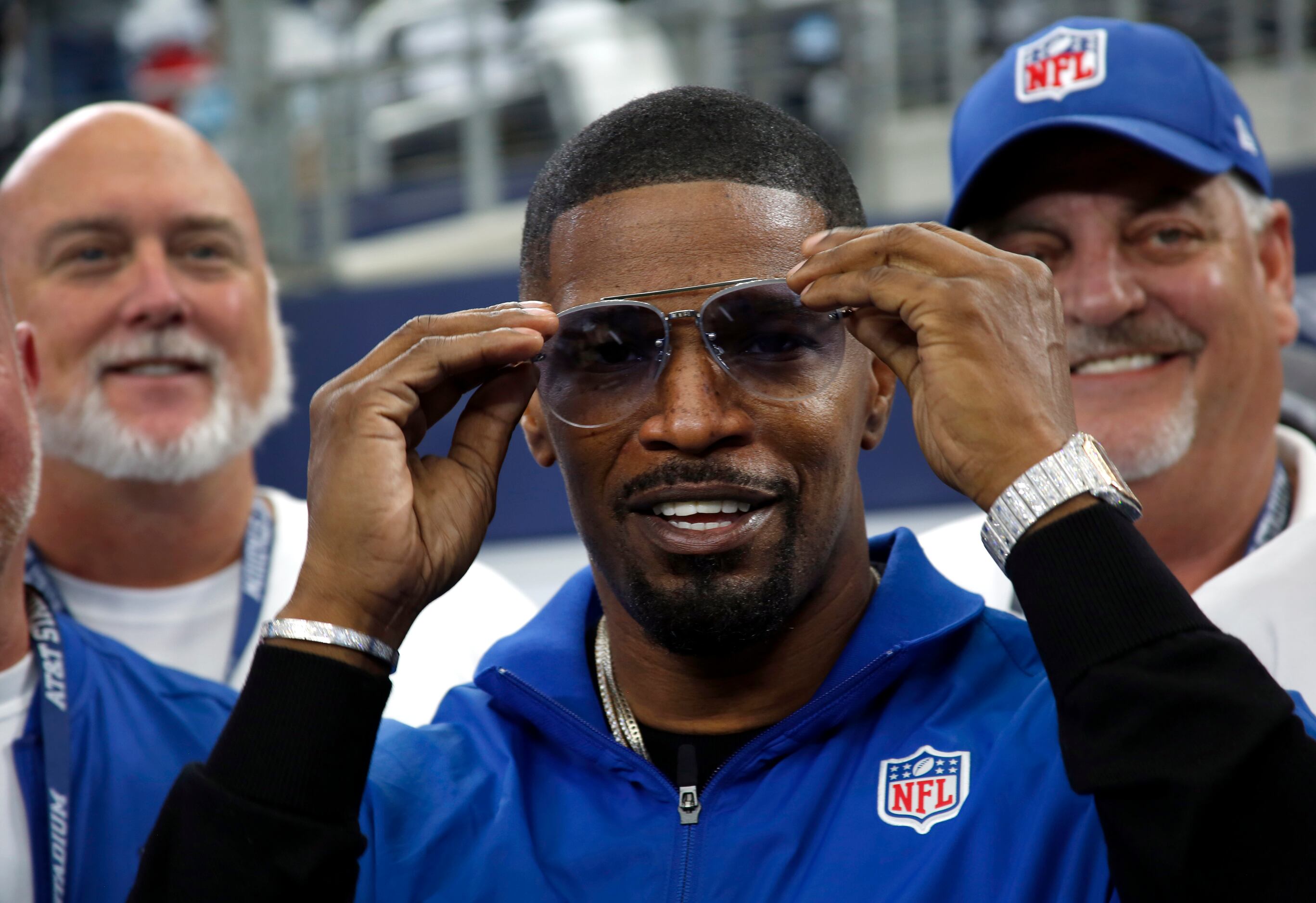 Actor Jamie Foxx adjusts his glasses as he poses with a photo with NFL game officials after...