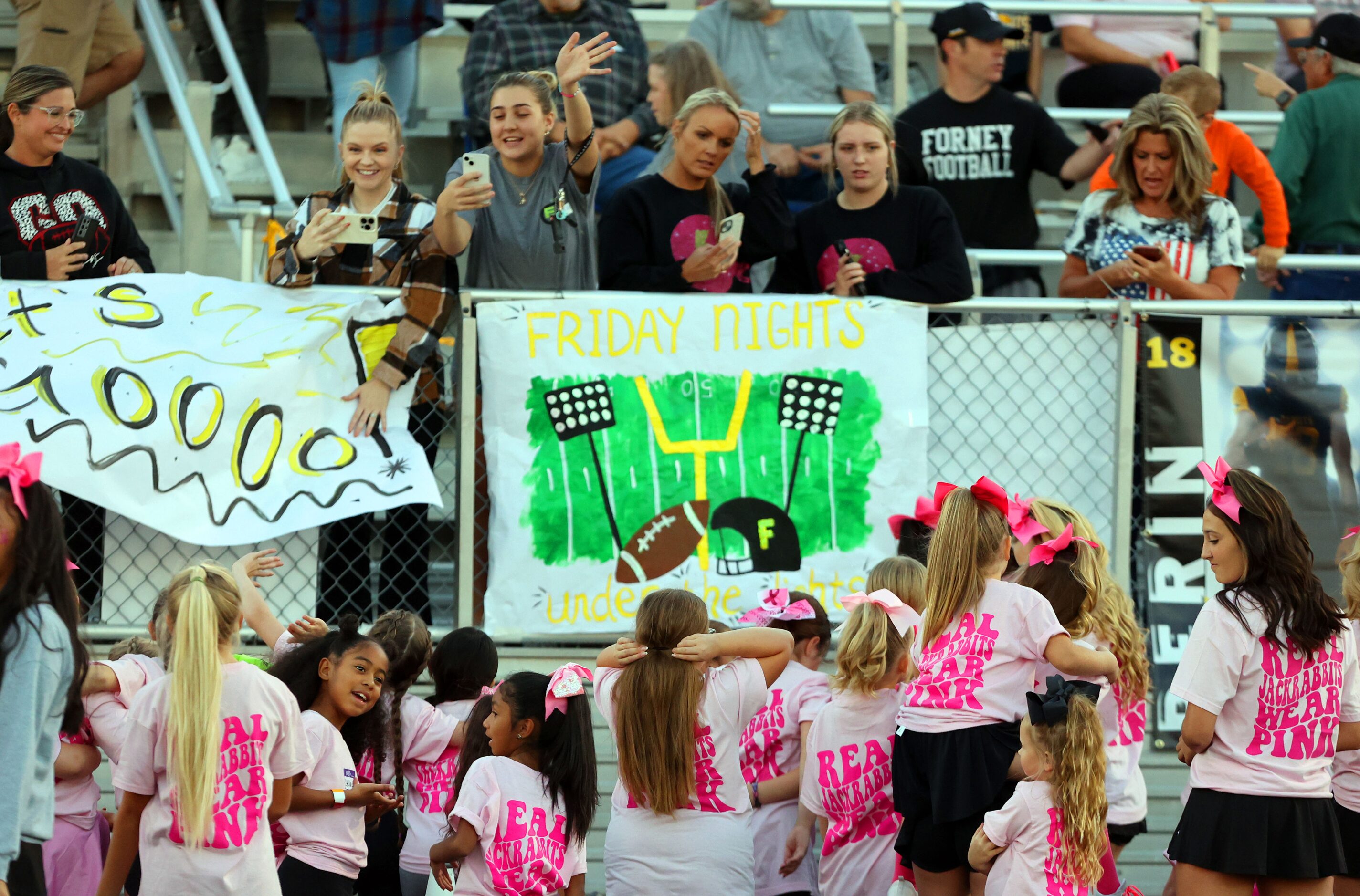 Moms wave to their junior cheerleader daughters before the first half of a high school...