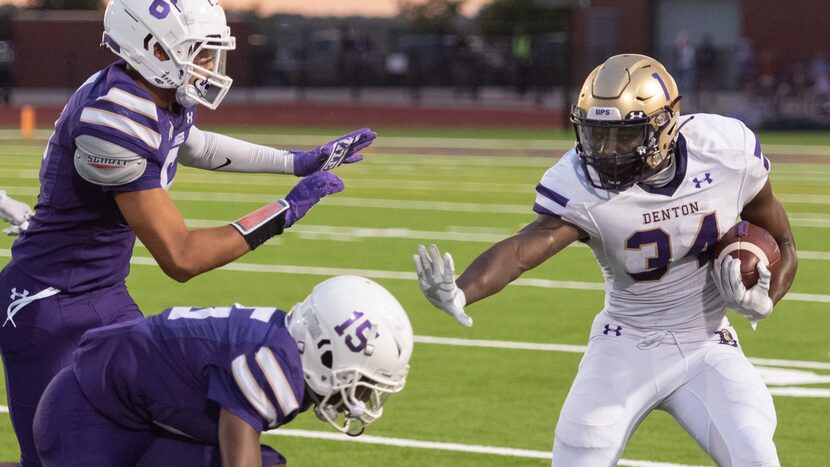 Denton High School RB Coco Brown throws a stiff arm during a football game.