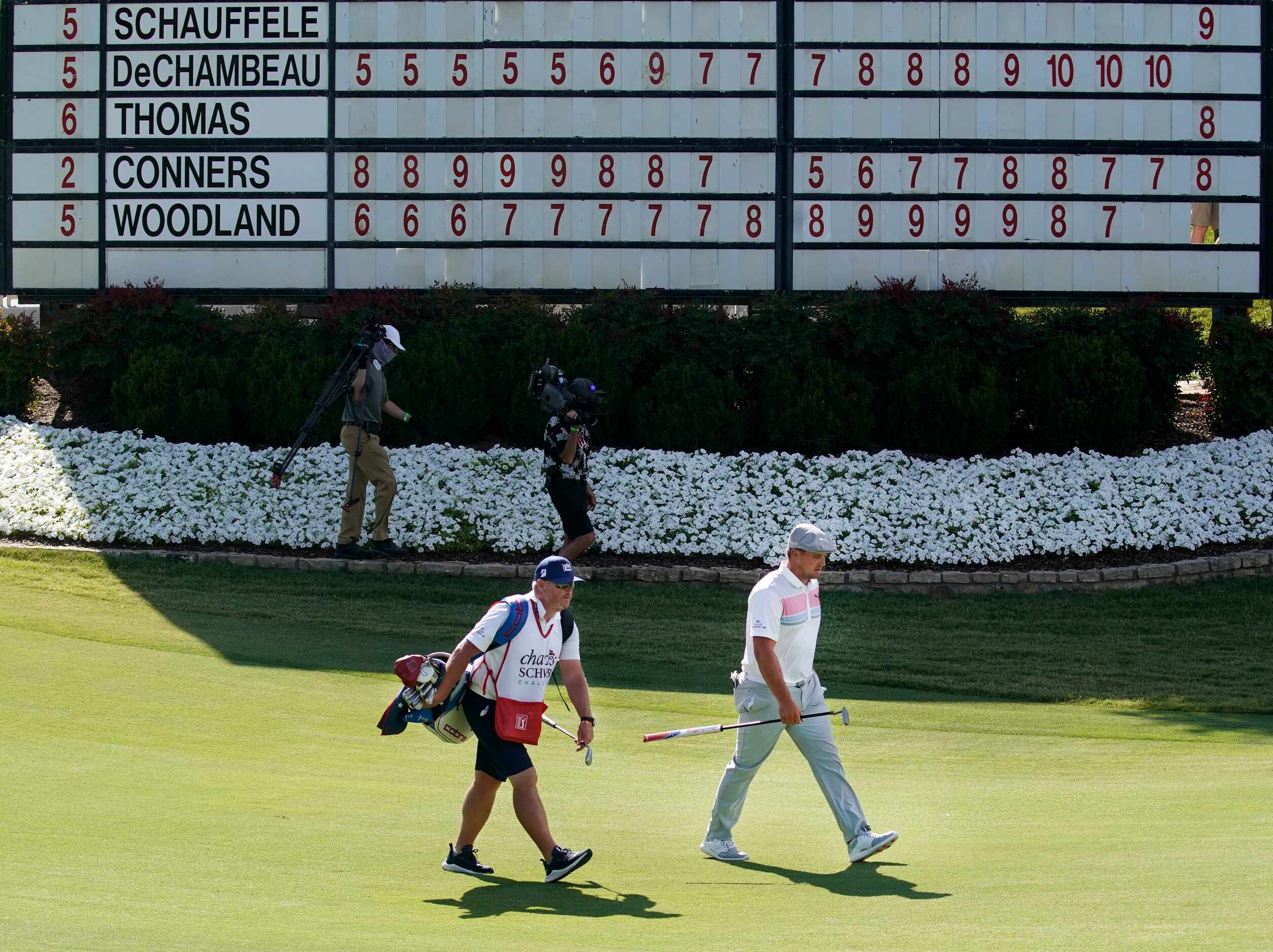 PGA Tour golfer Bryson DeChambeau (right) walks up the 18th fairway past the leaderboard...