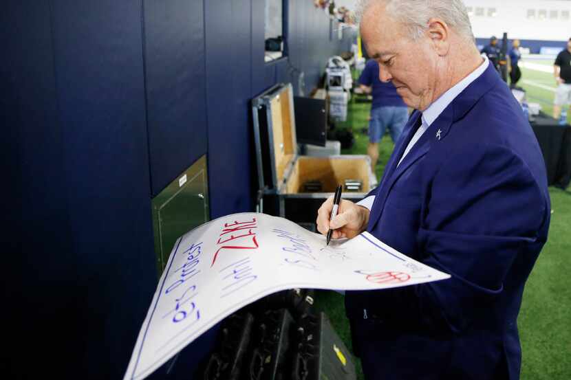 Dallas Cowboys executive vice president Stephen Jones signs items for fans before practice...