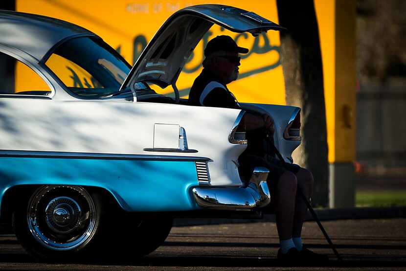 A parking attendant sits in the trunk of a vintage car after a spring training baseball game...