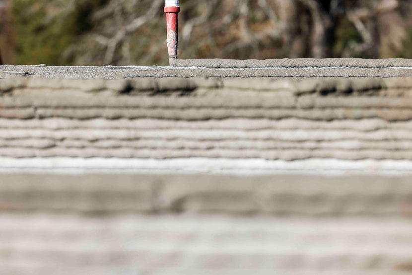 The nozzle of the 3D printer adds a layer of concrete on the walls of a self-storage...