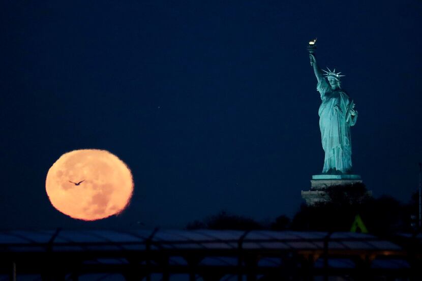 The supermoon appears near the Statue of Liberty, Monday, Nov. 14, 2016, in New York....