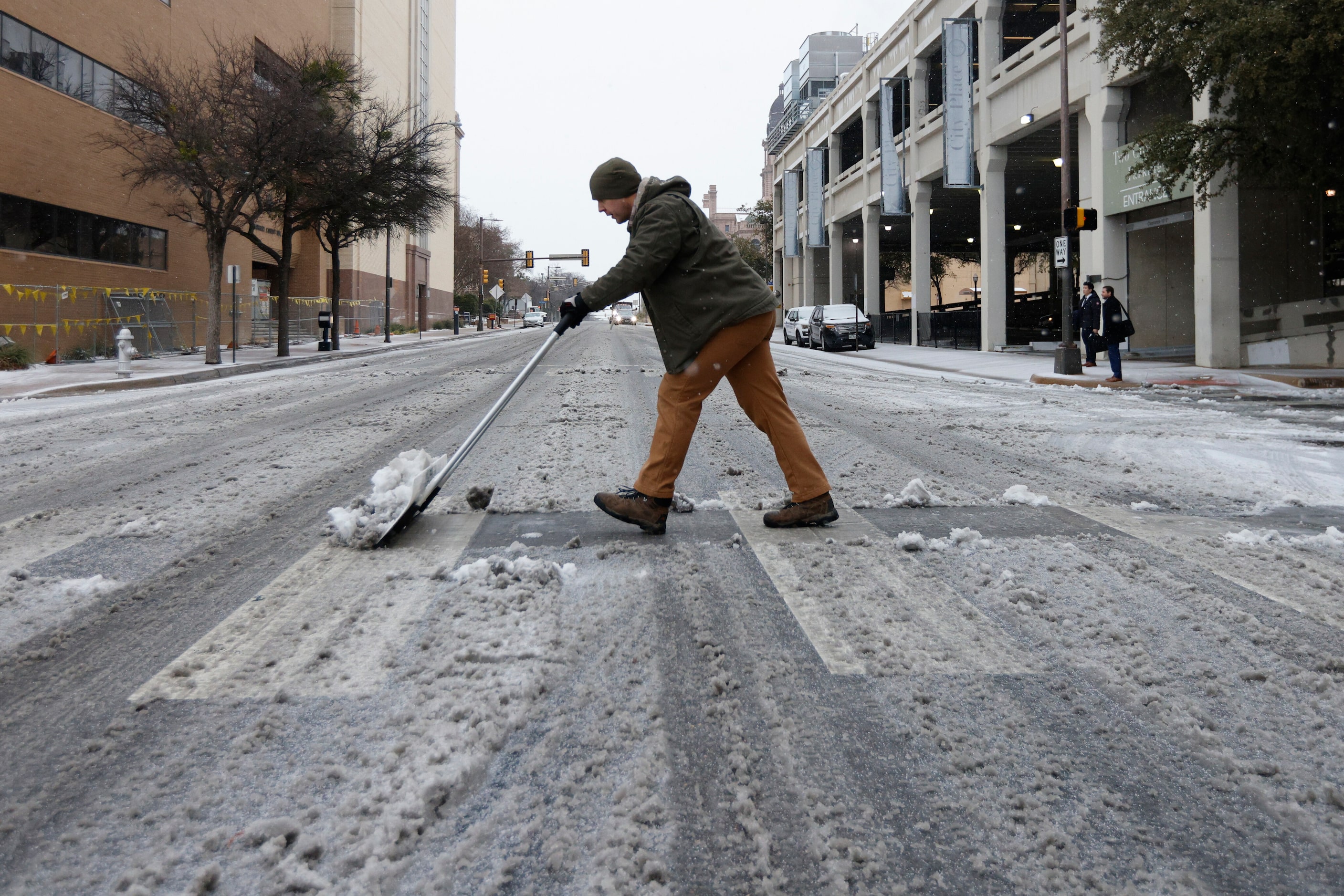 Derek Sutter, building manager for Tarrant County, shovels sleet and ice from a sidewalk on...