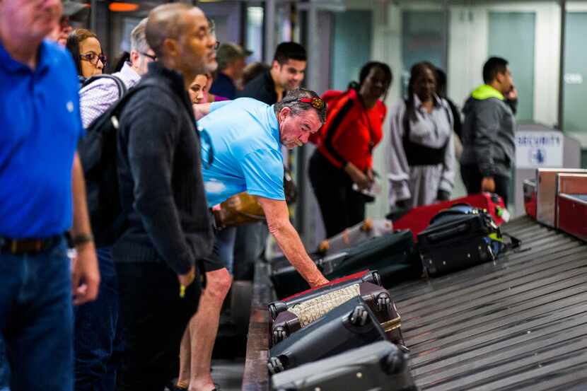 A traveler reaches for his bag as luggage moves around a baggage claim at Gate C on Friday,...
