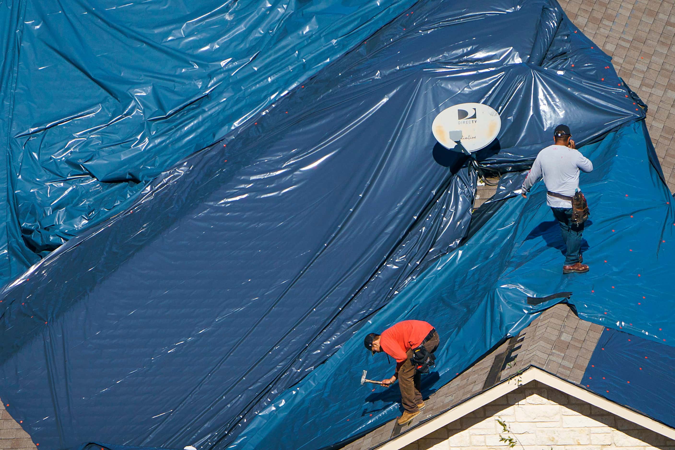 Workers install a tarp over a tornado damaged roof of a home near Walnut HIll Lane and Mash...