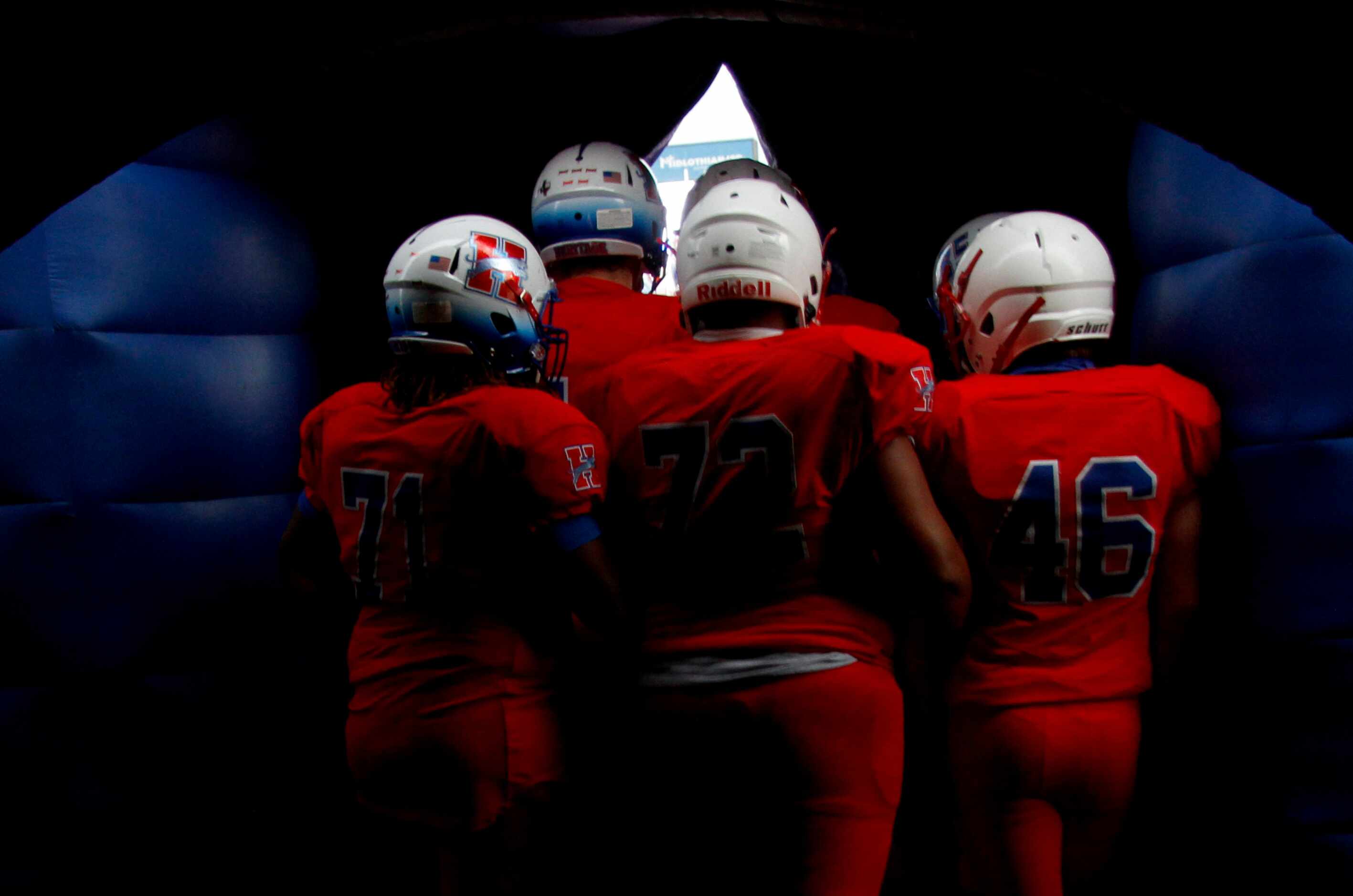 Midlothian Heritage players huddle and peek through an opening of their team inflatable...