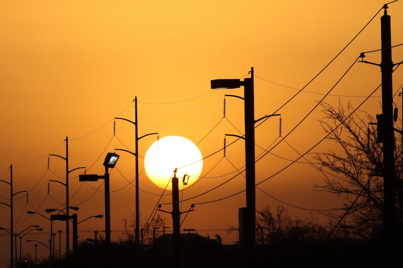 Overhead power lines and light poles are silhouetted as the morning sun rises over Camp...