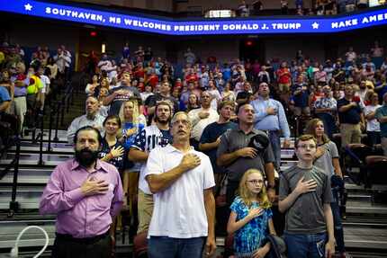 People stand for the national anthem before President Donald Trump speaks at a rally in...