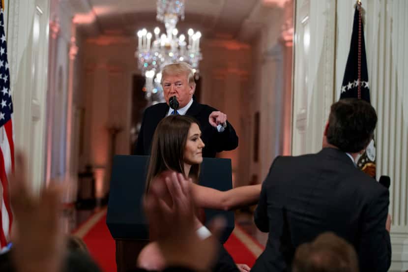 President Donald Trump watches as a White House aide reaches to take away a microphone from...