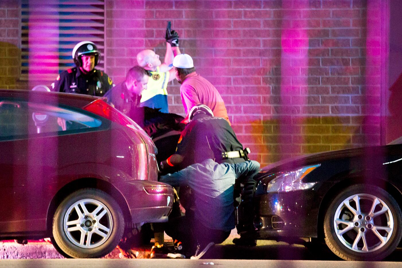 Shetamia Taylor (hunched over, in dark shirt, center), who was shot in the leg, is helped by...