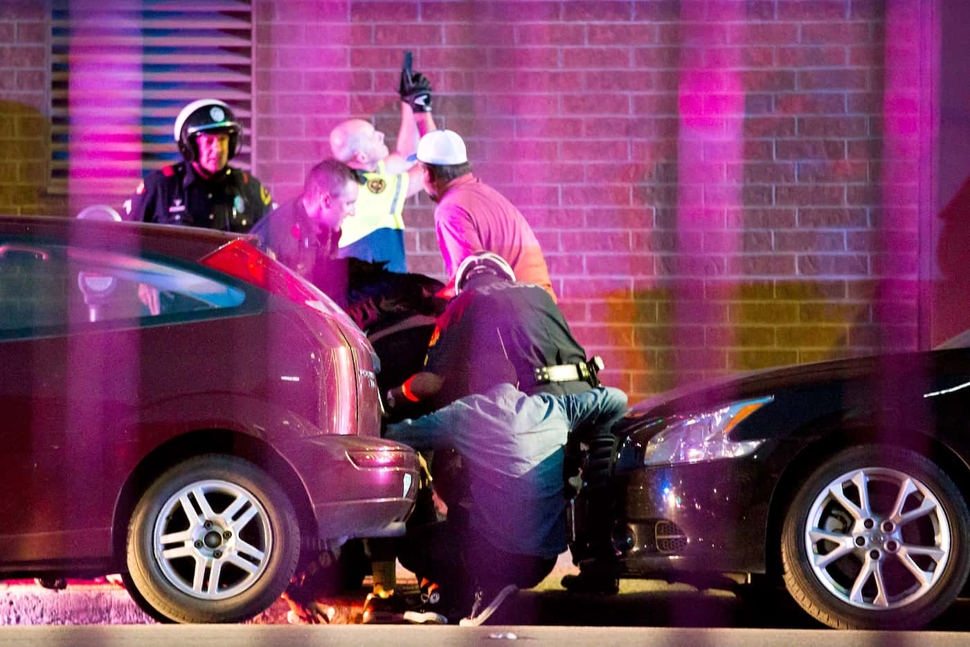Shetamia Taylor (hunched over, in dark shirt, center), who was shot in the leg, is helped by...
