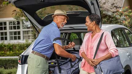 Older couple smiles at each other while loading the car's trunk with bags for a trip.