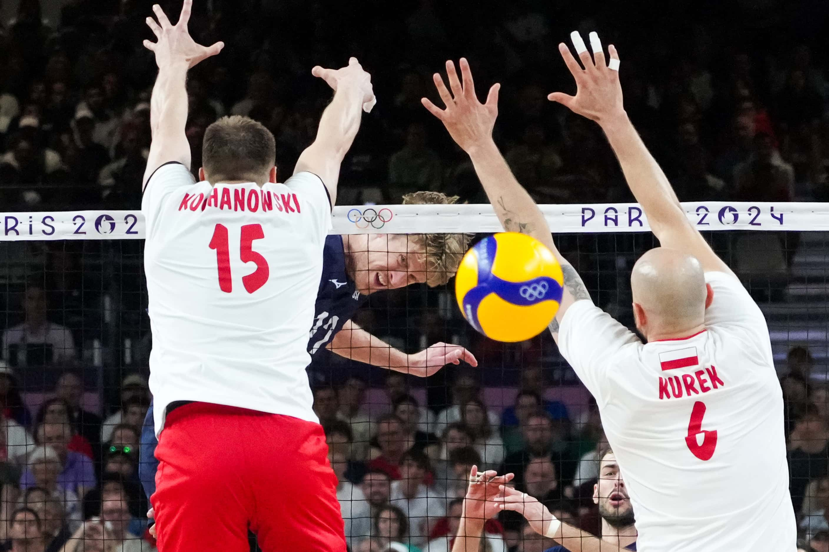 Maxwell Holt (12) of the United States hits through the block of Jakub Kochanowski (15) and...