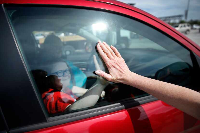 Volunteer Karen Kirk gives a student a high-five through the window after they made their...