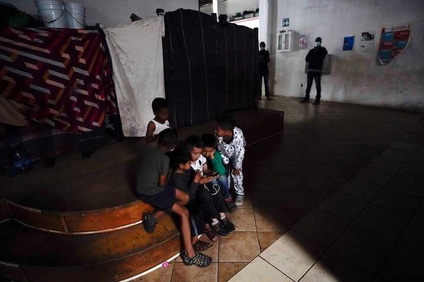 Children play a game on a cell phone in a shelter for migrants, May 23, 2022, in Tijuana,...