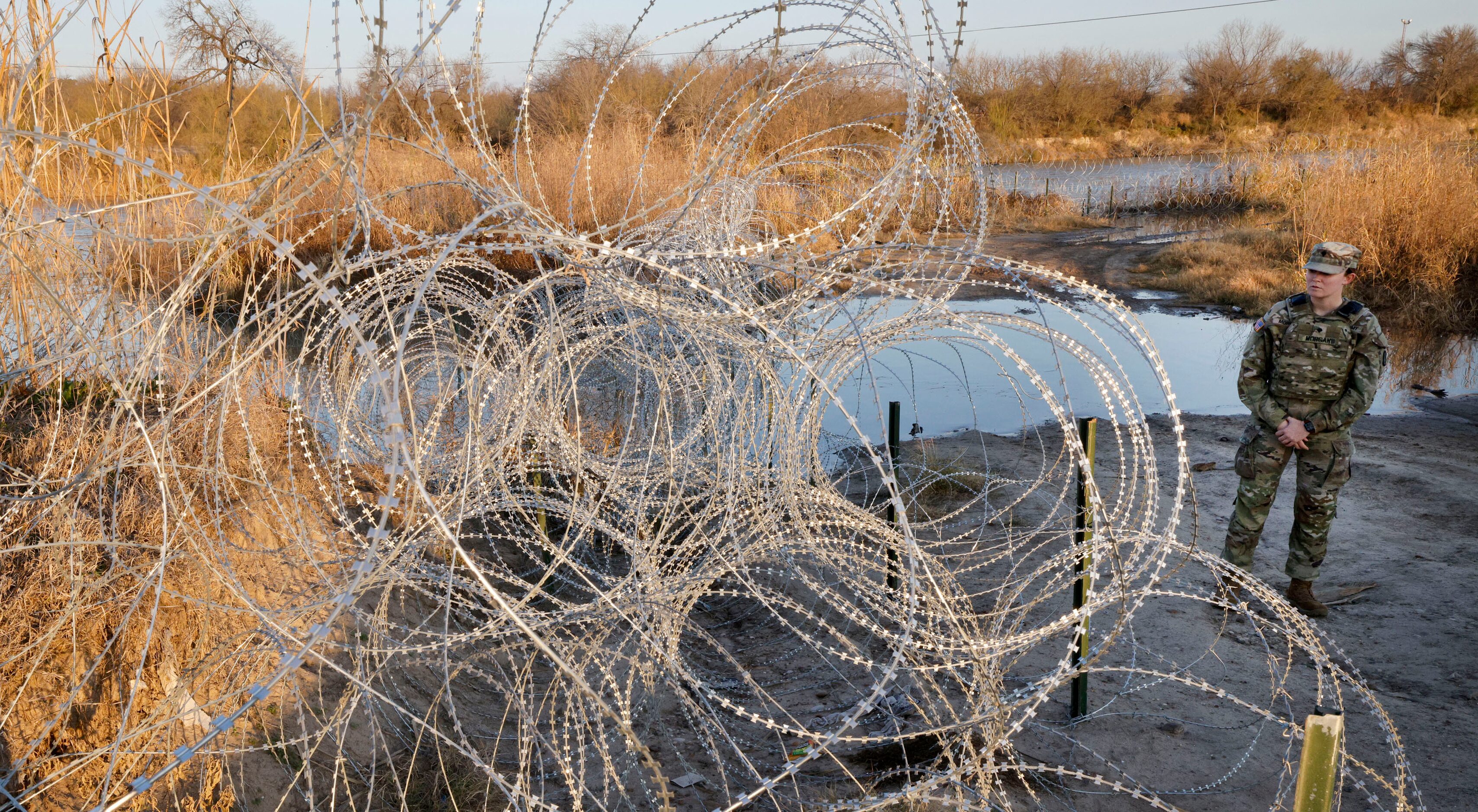 Texas National Guard Spc. Victoria Morgan stands by razor wire along the Rio Grande at...