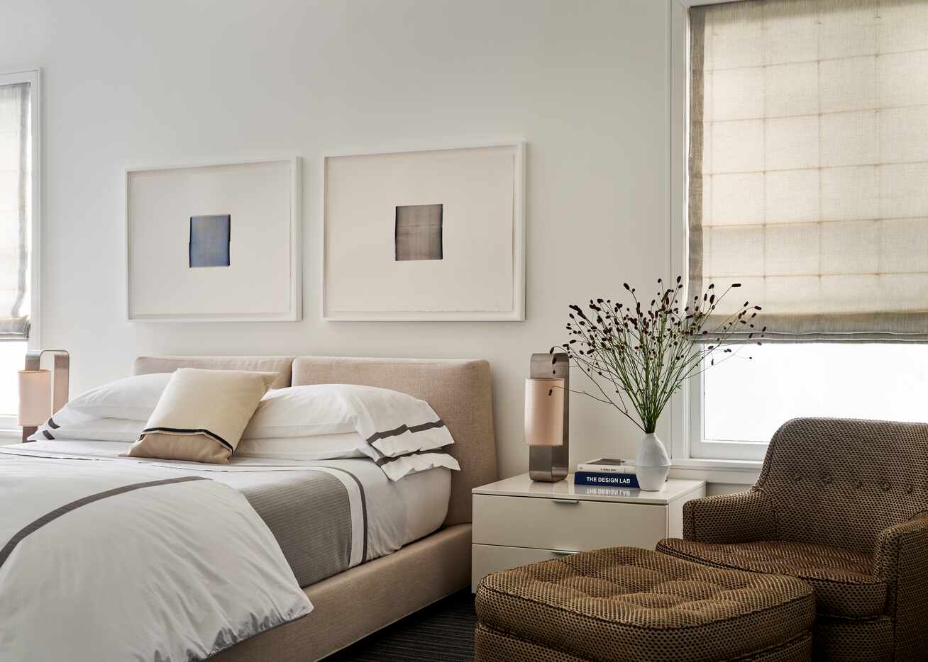 In a bedroom, two framed art pieces hang over the bed and a chair sits adjacent to the...