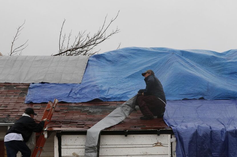 
Oscar Garcia (left) climbs a ladder to help Rocky Haddick cover his damaged roof on his...