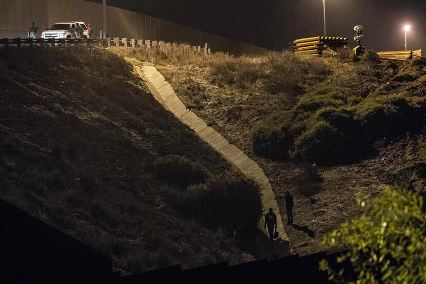 Border Patrol agents look for Central American migrants hiding on the U.S. side of a fence...