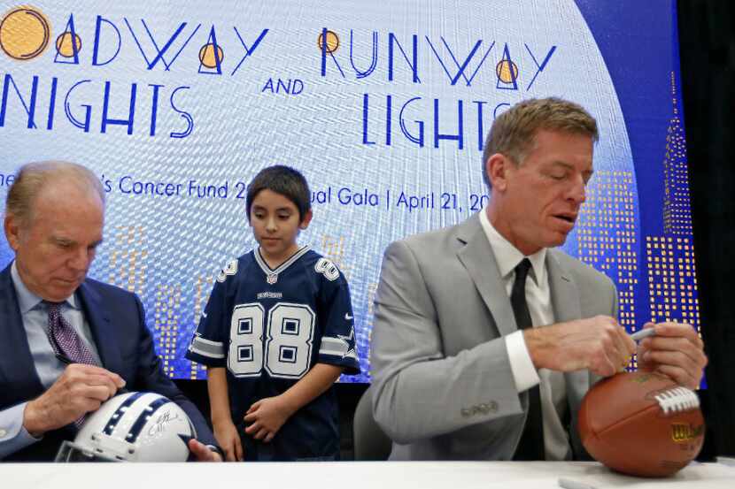 Roger Staubach (left) signs autograph for Cowboys fan Jesus Martinez (center), 11, next to...