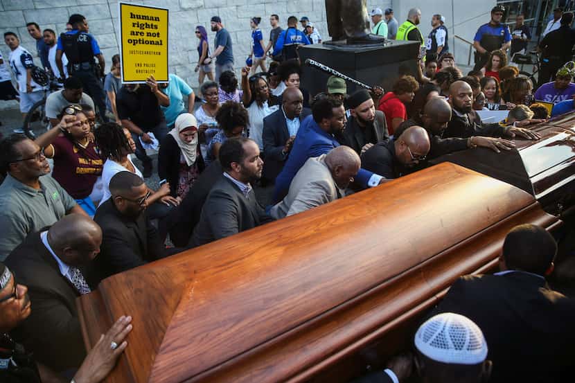 Members of the clergy and community kneeled  around two empty coffins  during a protest...