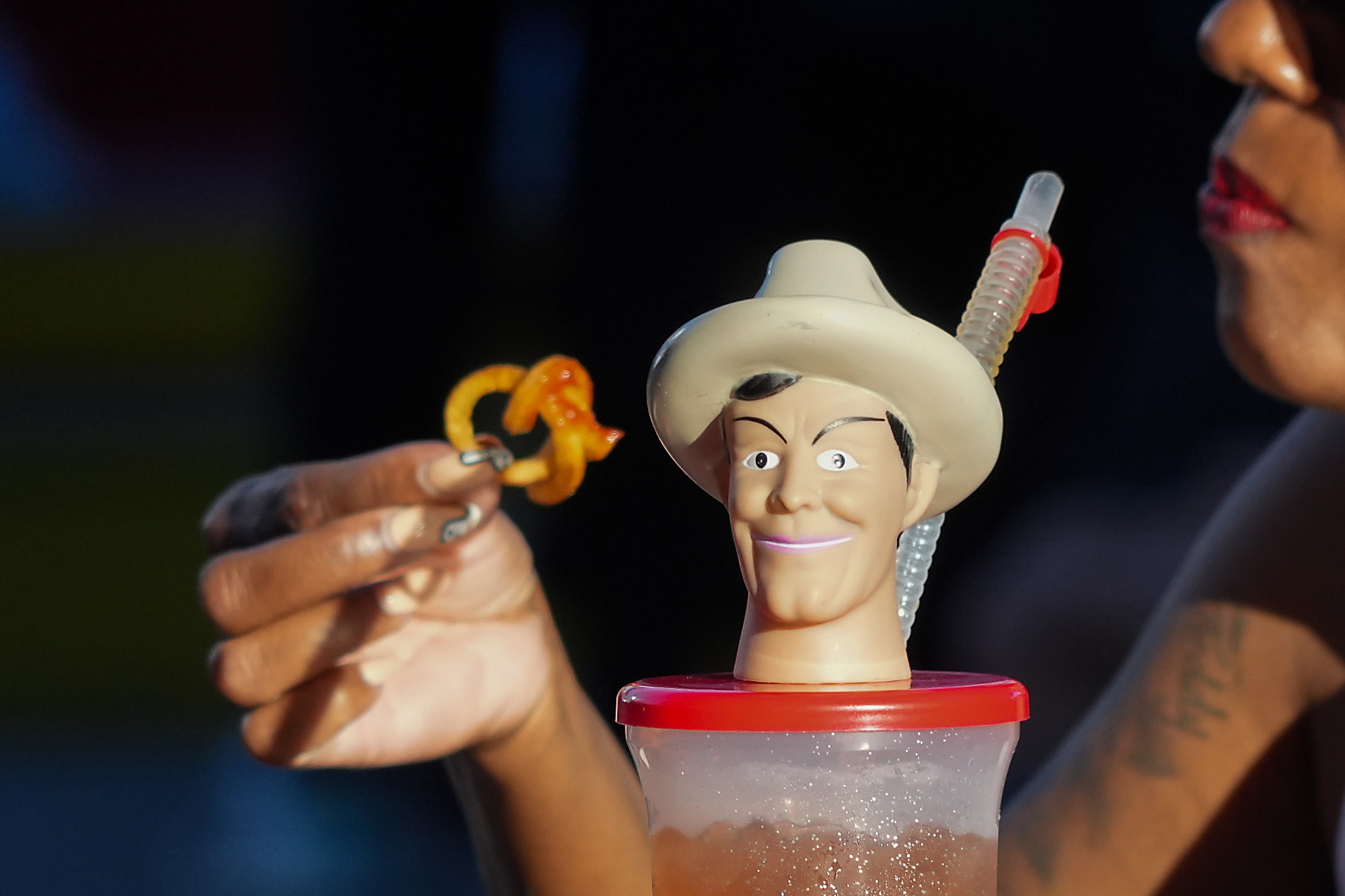 A fairgoer eat curly fries behind a Big Tex souvenir cup at the State Fair of Texas on...