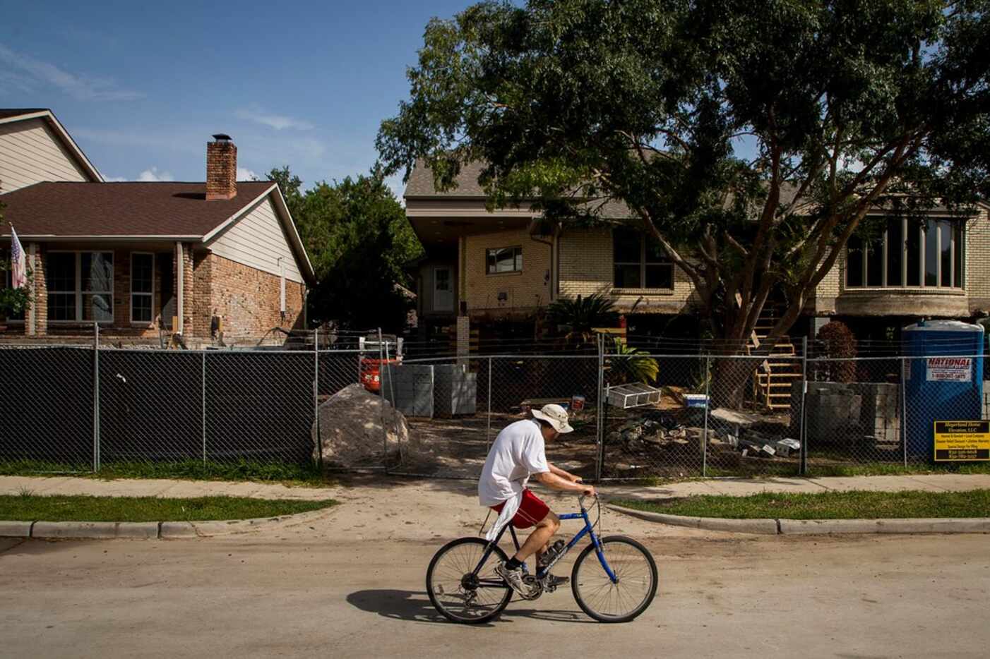 A cyclist rides past houses being raised as part of home elevation efforts in the Meyerland...
