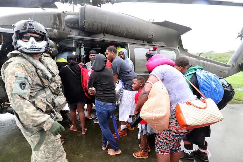 Evacuees board a waiting National Guard Black Hawk helicopter on the basketball court of...