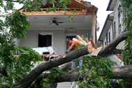 A man uses a chainsaw to cut up a tree that tore off the facade of a house, Friday, May 17,...