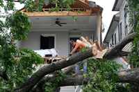 A man uses a chainsaw to cut up a tree that tore off the facade of a house, Friday, May 17,...