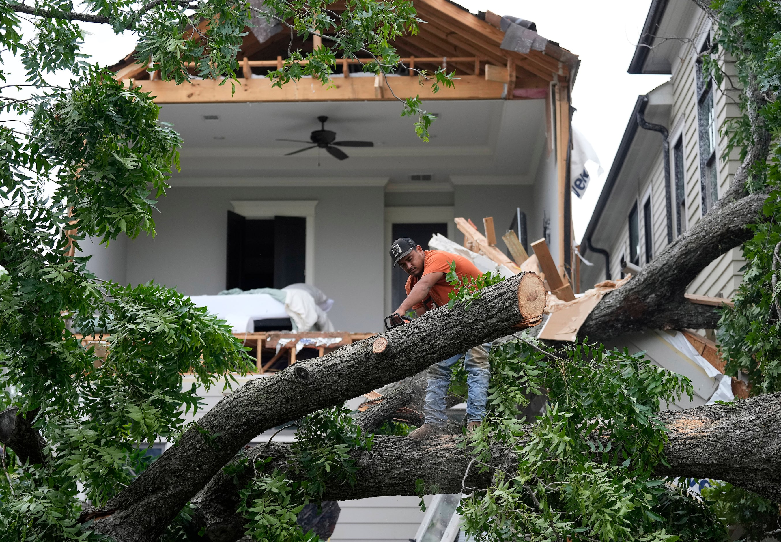 A man uses a chainsaw to cut up a tree that tore off the facade of a house, Friday, May 17,...