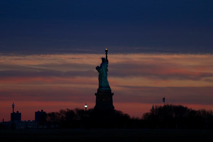 The setting sun lights up the sky over the Statue of Liberty viewed from Liberty State Park,...