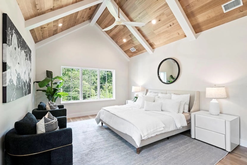 Bedroom with wood-beam ceiling, white bed and nightstand, black accent chairs