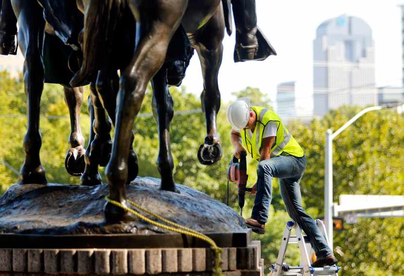 A crewman from Howell Crane and Rigging Inc. drills into the base of the statue has they had...