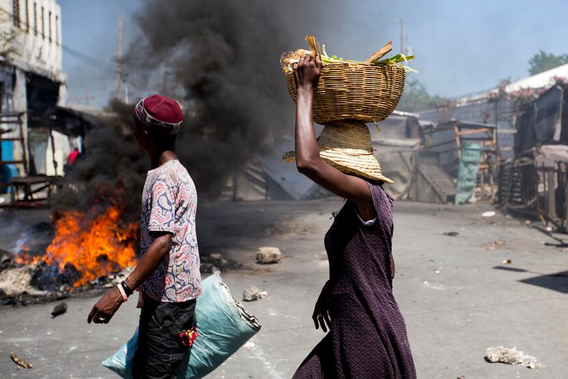Street vendors walk past burning tires set up by anti-government protesters during a general...
